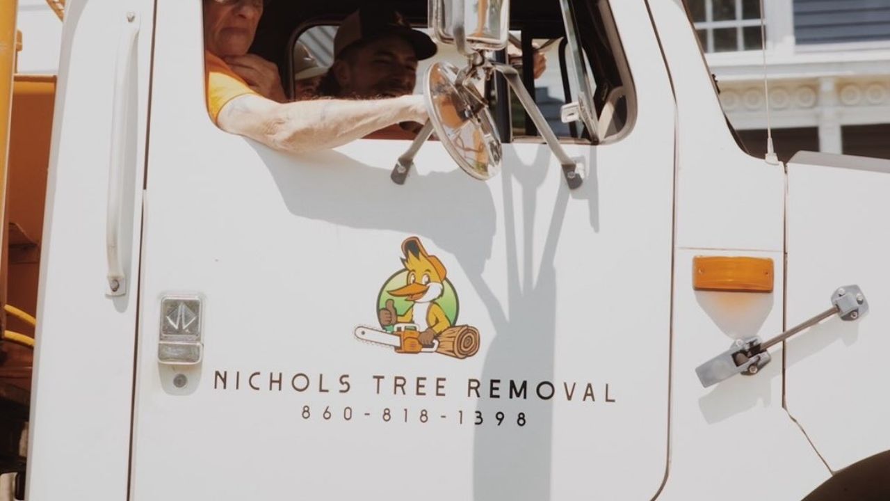 The door of the Nichols Tree Removal bucket truck with the logo, the name and the phone number, a crew member at the wheel.
